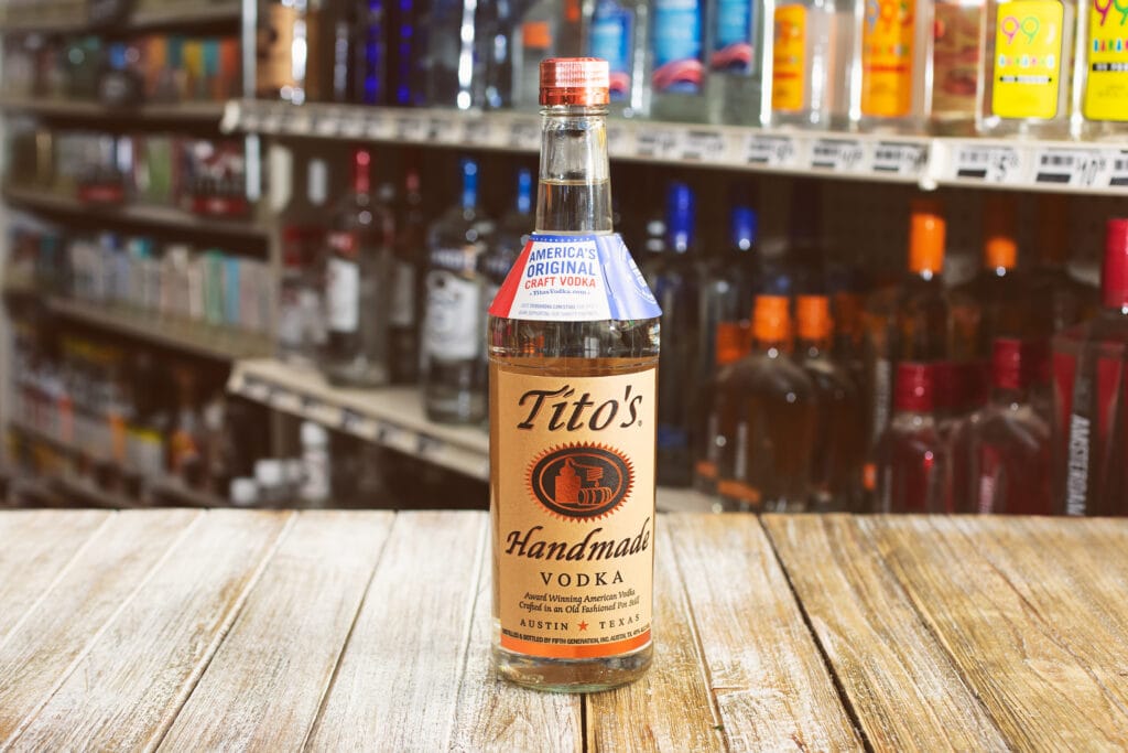 view of a bottle of Tito's Vodka, on a wood table, in a liquor store setting